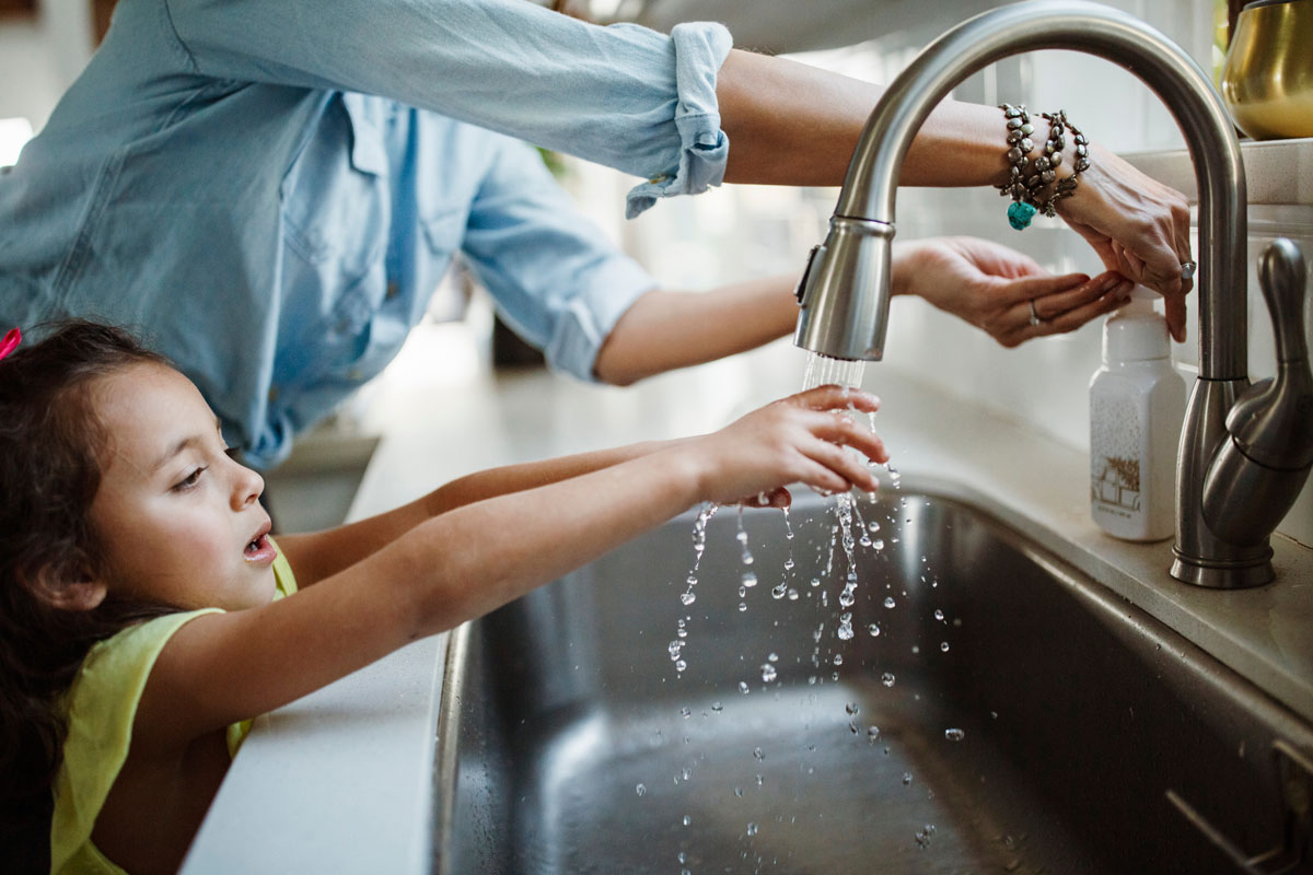 A mother with daughter washing hands in sink at home